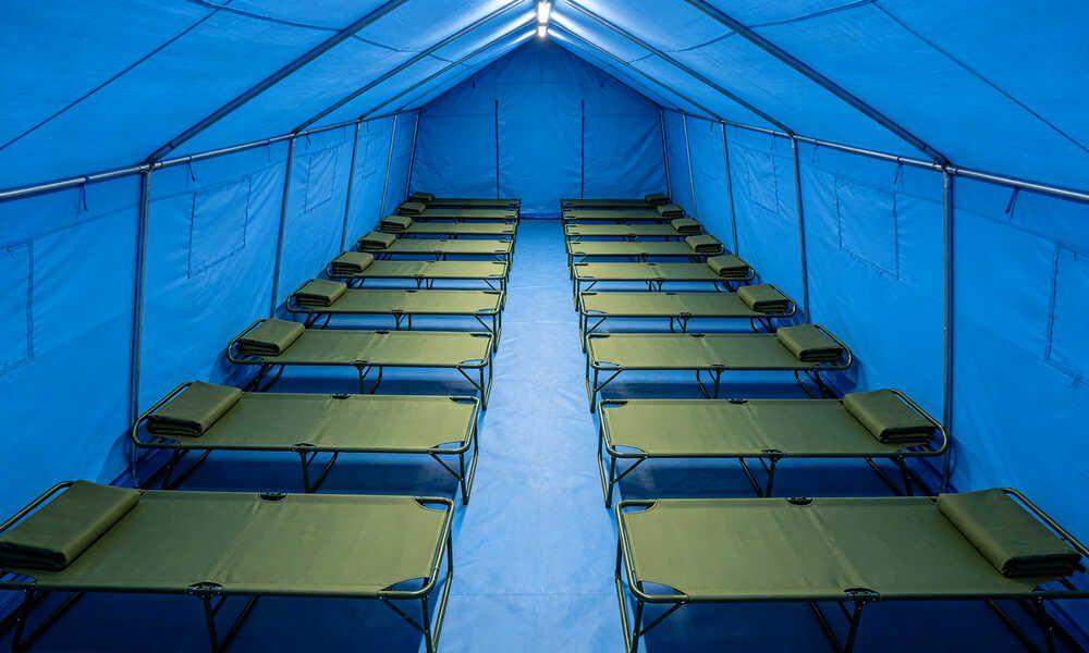 Top‑view interior layout of blue emergency frame tent with neat rows of folding cots and central walking aisle for disaster shelter occupancy