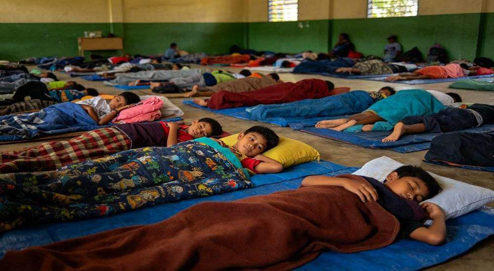 Wide angle view of Southeast Asian school emergency shelter students resting on sleeping bags classroom