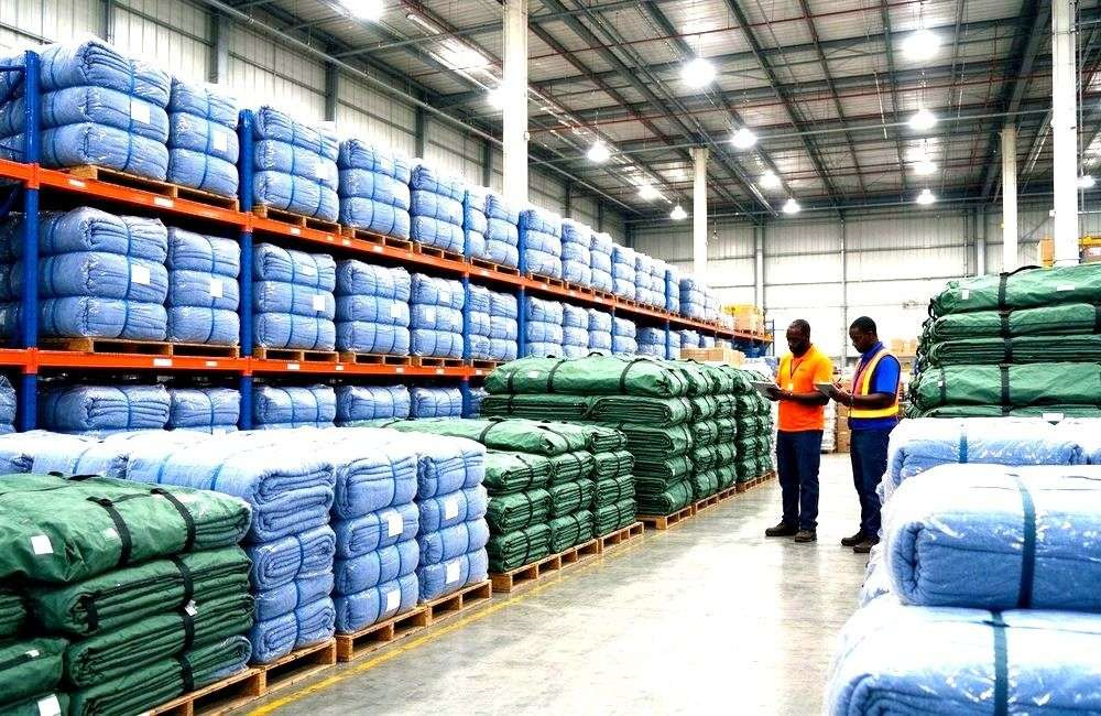 Warehouse shelves stacked with blanket bales ready for cyclone response in the corridor, showing bulk cyclone relief supplies for storm programs